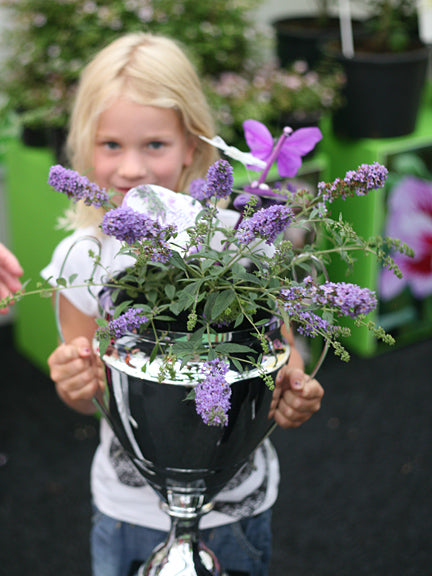 A young girl holds a silver trophy cup with a Lo and Behold Lilac Chip butterfly bush in it